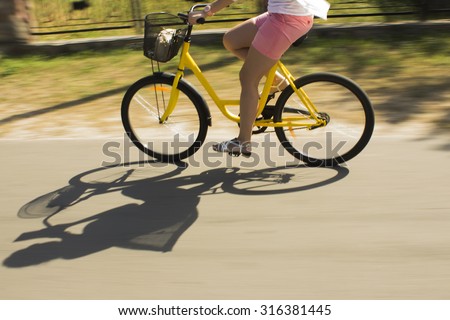 Motion blur.Riding yellow bicycle on the forest road. Close-up of young woman riding bicycle