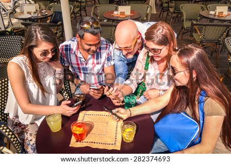 Group of young hipster friends having fun together with smartphone at restaurant bar - Technology concept of interaction in everyday lifestyle - Internet connection spot outdoor - Sunny day color tone