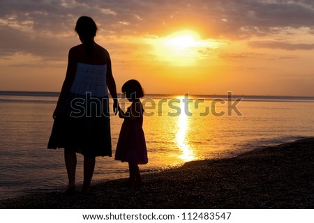 Mother and kid silhouettes on sunset beach, family summer vacation