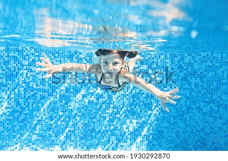 Little child swims underwater in swimming pool, happy active girl dives and has fun under water, kid fitness and sport 
