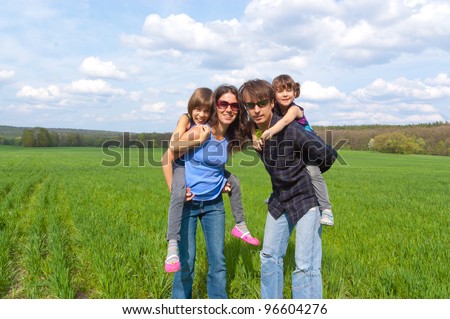 Happy family outdoors having fun. Active parents giving their kids piggyback ride. Father, mother and children on family vacation.