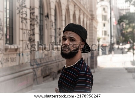 Young black brazilian man with beard, striped t-shirt, cap, ring and pearl chain in downtown São Paulo Imagine de stoc © 