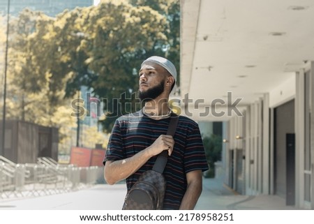 Young black brazilian man with beard, striped t-shirt, bag, durag, ring and pearl chain standing watching something in the streets of downtown São Paulo Imagine de stoc © 
