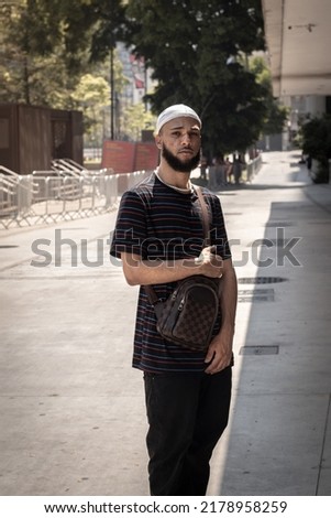 Young black brazilian man with beard, striped t-shirt, bag, durag, ring and pearl chain standing on the streets of downtown São Paulo Imagine de stoc © 
