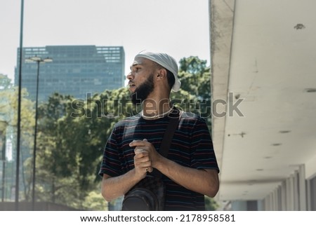 Young black brazilian man with beard, striped t-shirt, bag, durag, ring and pearl chain standing watching something in the streets of downtown São Paulo Imagine de stoc © 