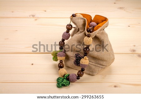 Crochet necklace handmade crochet leaves and acorns and round dark brown wooden beads in jute bag on a light wooden board