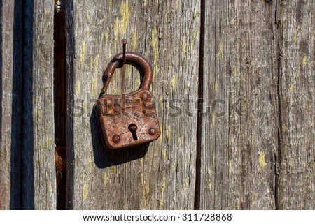 Rusty padlock hanging on a rusty nail in the wooden wall of summertime in the village