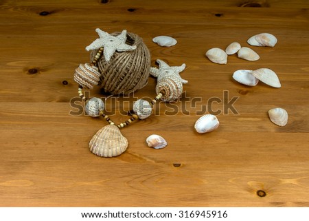 Handmade crochet white-beige beads with natural sea shells pendant and crocheted starfish, seashells and a skein of twine on a wooden table
