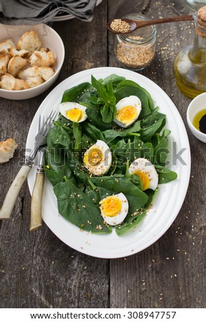 Salad with spinach, eggs and sesame seeds served with toasted white bread and olive oil on a white oval plate on wooden background