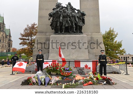 OTTAWA - OCT 25, 2014:  Sentries stand at attention while mourners pay respect at the Ottawa Cenotaph where guard Nathan Cirillo was shot 3 days before.  An armed policeman, left, is also on site.