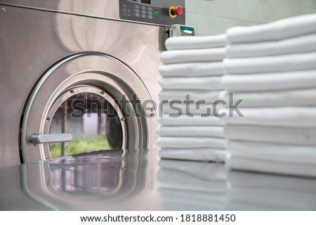 Stack of clean bed sheets in front of industrial washing machine. Focused on washing machines. 
Shot taken in the factory.