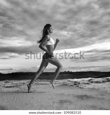 Running bare-feet woman. Female runner jogging during outdoor workout on sand at evening. Beautiful Fitness model outdoors.