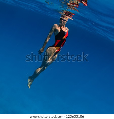 professional sport swimmer floating up underwater in blue with small air bubbles on her face