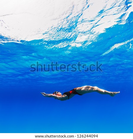 professional female swimmer moving on her back underwater in blue