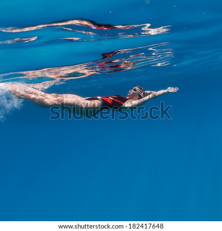 Professional female swimming on her back underwater in blue with mirror on water surface and caustic effect on her skin