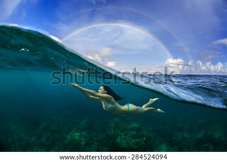 Underwater Sport Postcard. A freediver floating under water surface in ocean. A rainbow appear on cloudy sky over beautiful seascape