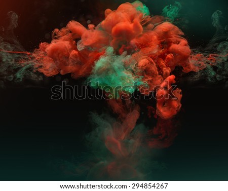 Red and green complementary colors in clouds. Colorful ink and paint swirling underwater on dark background.
