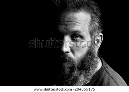 A Black and white portrait of a bearded man in front of a black background. High Contrast.