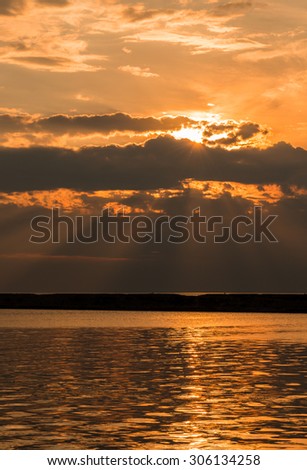 The Sun shines through a break in the clouds at dusk over a harbor break wall.