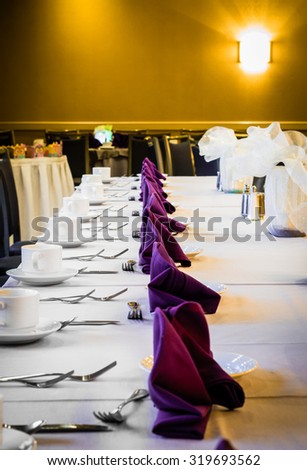 A formal Table Setting on a white tablecloth for a dinner with silverware, coffee mugs, forks, and knives.