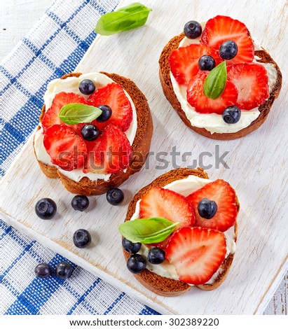 toasted bread with cream cheese and berries on wooden cutting board, top view