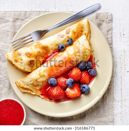 plate of crepes with fresh berries and sweet sauce, top view