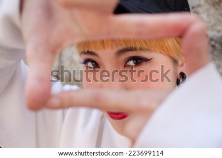 Portrait of a Japanese woman with orange hair as she is framing her face with her own hands.