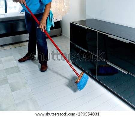Housekeeper sweeping bedroom floor under the dresser