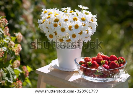 bowl of fresh strawberries and bouquet of camomiles on table in the garden