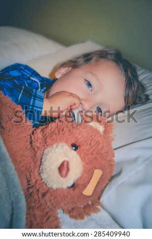 Sick child with a thermometer in his mouth and in bed with his teddy bear.