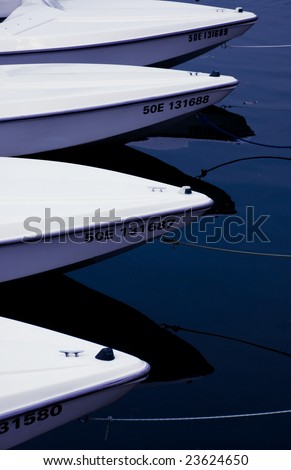 Four ports of white boats float on blue water.  Rope is tied to the boat and goes off the frame.