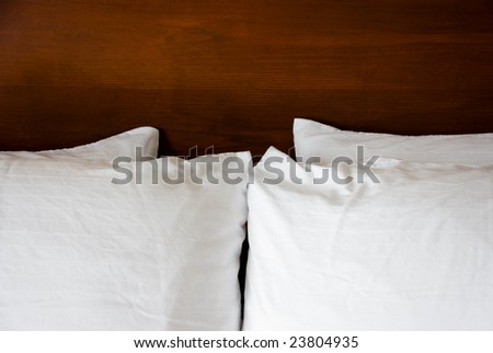 Four white fluffy pillows lay symmetrically against a solid wood stained headboard.