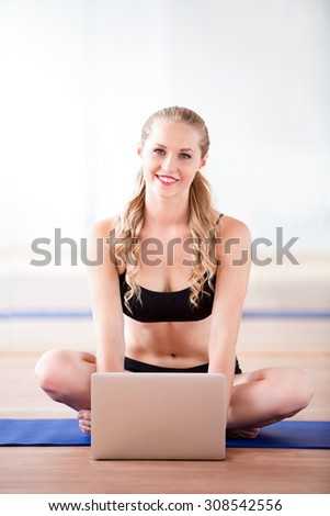 A happy girl sits while training and looking at a laptop. She is find a new exercise.
