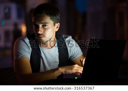 Man is sitting on the table with his computer. He is looking for us in the darkness. He was working