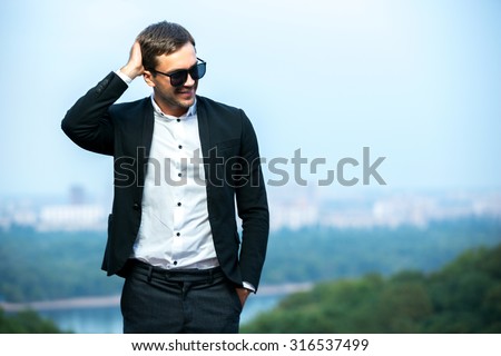 Dress code wearing man is smiling and scratching his head. Skyline in background. Happy young man.