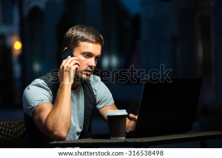 Male is working on the computer and talking on the iphone. Drinking coffee on a cafÃ?Â©. He found information that he needed.