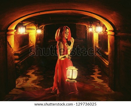 Romantic brunette holding a lantern in a dark dungeon