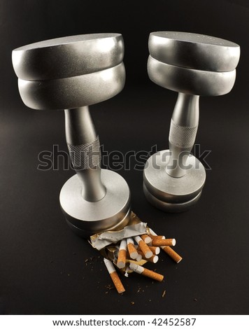pack of cigarettes crushed metal dumbbell on a black background. Sports wins bad habits.