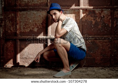 young fashion man squat against old rusty wall