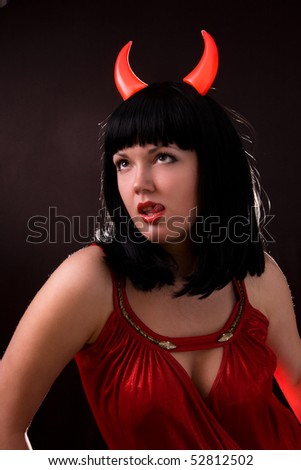 Sexy Halloween devil girl witch on dark background. Beautiful woman with Devil horns. Portrait of young woman dressed as pretty devil.Sexual Young Woman in a Costume of Red Female Devil