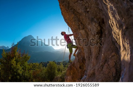 Athletic man climbs an overhanging rock with rope, lead climbing. silhouette of a rock climber on a mountain background. outdoor sports and recreation