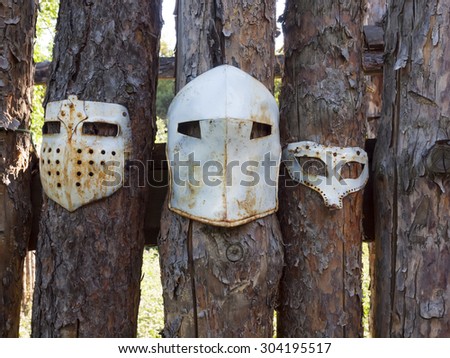 Medieval iron mask hanging on the fence of logs.