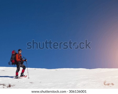 A guy with a large backpack and snowshoe walking through the mountains in winter.