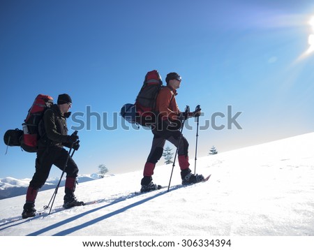 Friends in snowshoes and big backpacks are traveling through the mountains in winter.