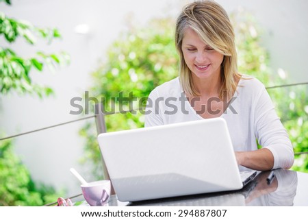 beautiful woman working on a computer at home with green garden on her background