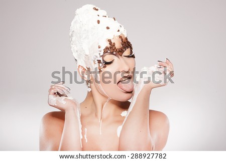 Portrait of beautiful girl with trendy make-up with coffee beans and cream, licking her skin. Body painting.