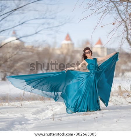 girl in a flowing blue dress dancing in the snow against the backdrop of an ancient castle