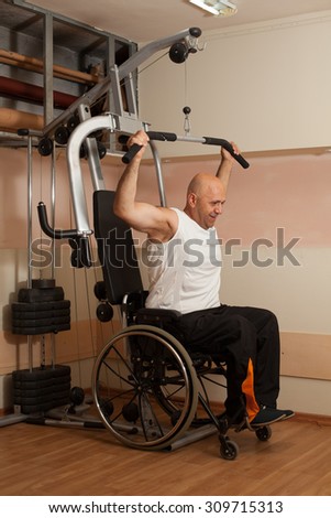 Happy disabled person in the gym doing exercises with training apparatus.