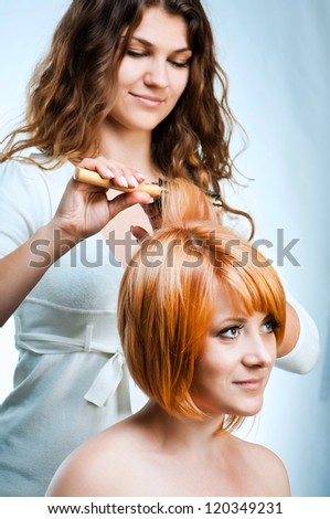 Young fashion woman hairdresser makes hairstyle for a girl isolated on white background