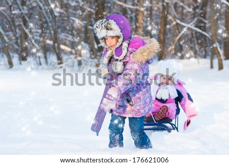Cute girl pulling sister on a sled through the snow